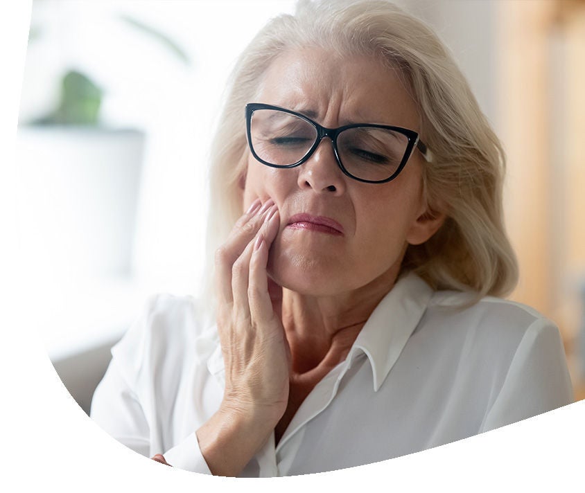 Starsza kobieta z bólu łapie się za policzek