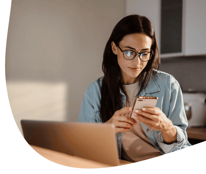 Kobieta patrząca na telefon, siedząc przed laptopem