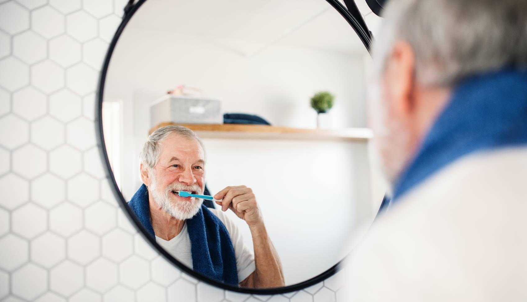 Starszy mężczyzna myje zęby przed lustrem
