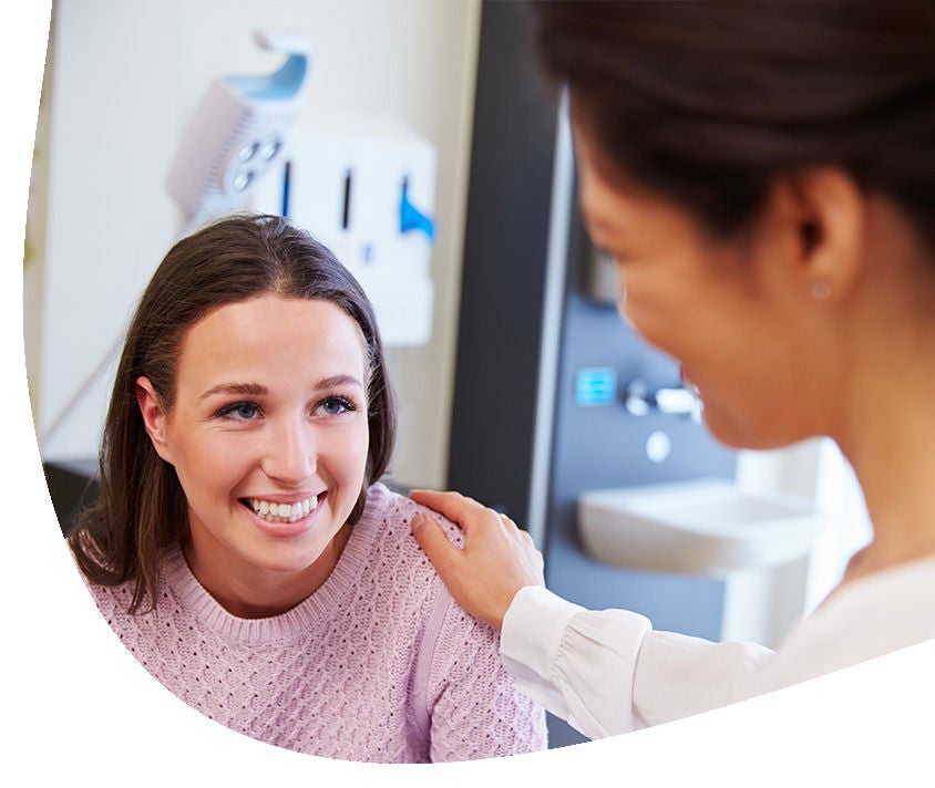 Uśmiechająca się kobieta siedzi w gabinecie dentystycznym, przed inną kobietą